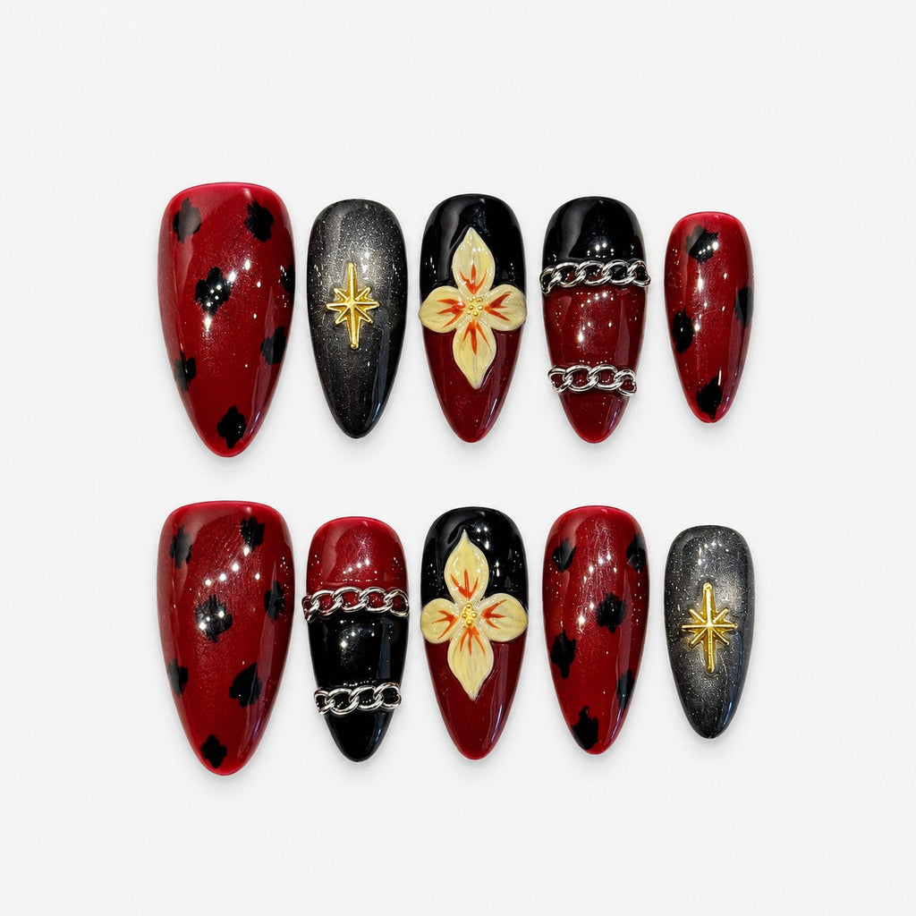 catalog: Medium almond press-on nails in dark wine red and black with painted cream orchids, black spots, a gold star charm and raised silver chains.