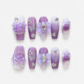 catalog: Medium coffin press-on nails in white to lilac ombre with sculpted purple flowers, silver glitter and clear rhinestones.